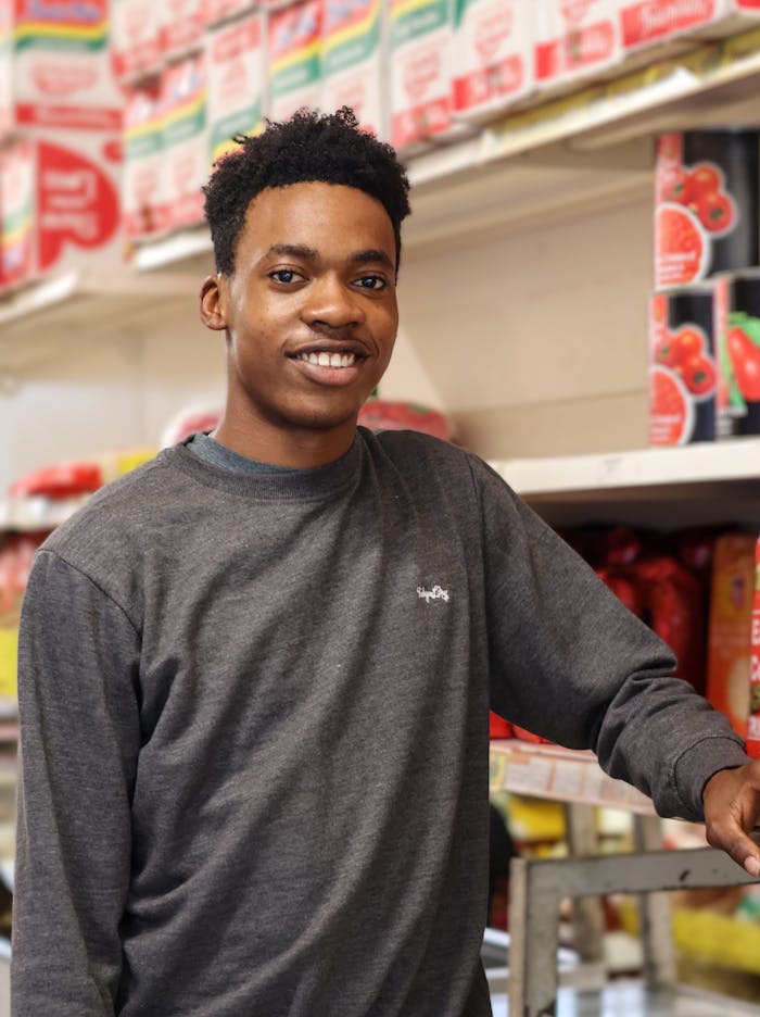 A smiling young adult man in a grocery store aisle surrounded by colorful product packaging.