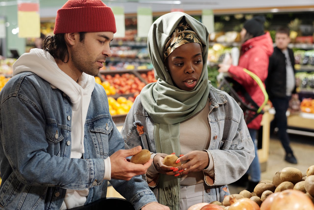 about-us A diverse couple selecting fresh kiwis in a vibrant supermarket produce section.